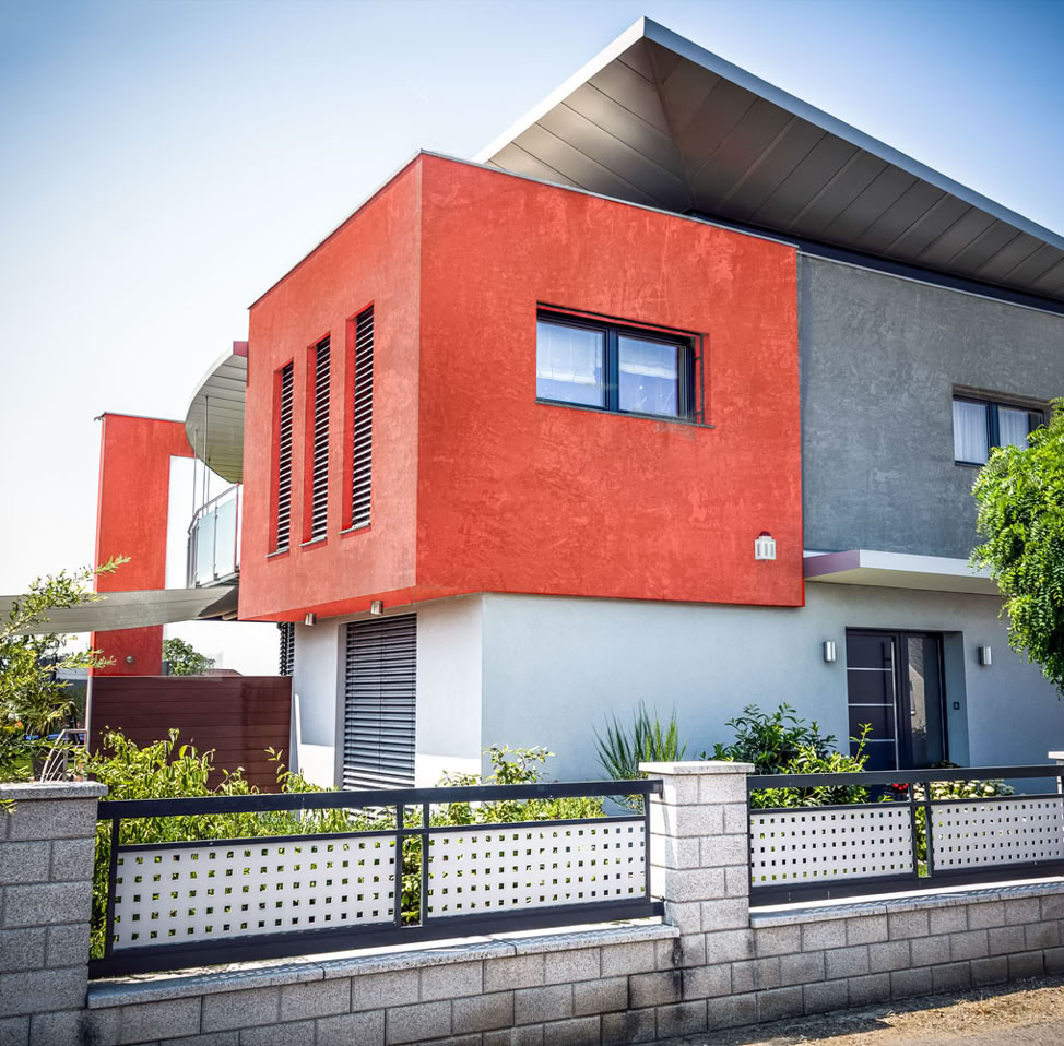 Das Bild zeigt eine moderne Fassade eines Hauses, versehen mit glamur Kalk-Marmor-Beschichtung, die durch mineralische Pigmente in sanften Rot- und Grautönen changiert. Diese natürliche Farbgebung betont die zeitgemäße Architektur und verleiht der Fassade eine elegante, lebendige Ausstrahlung.