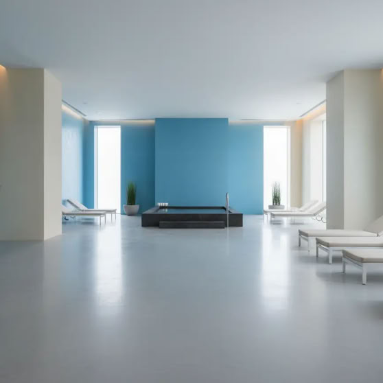 Ein moderner, heller Raum mit blauen Wänden, weißen Liegestühlen, großen Fenstern und Pflanzen in Töpfen.